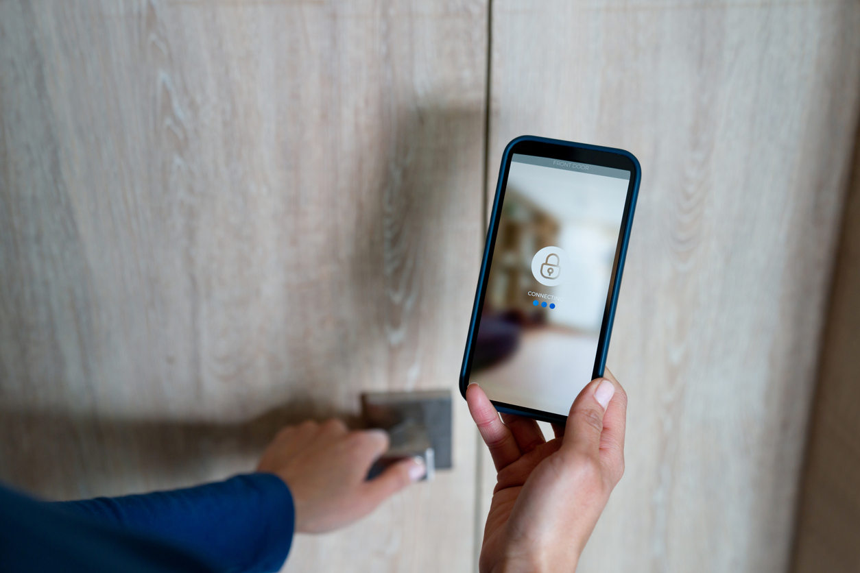 Close-up on a woman opening the door of her house using a home automation system on her cell phone - smart homes concepts